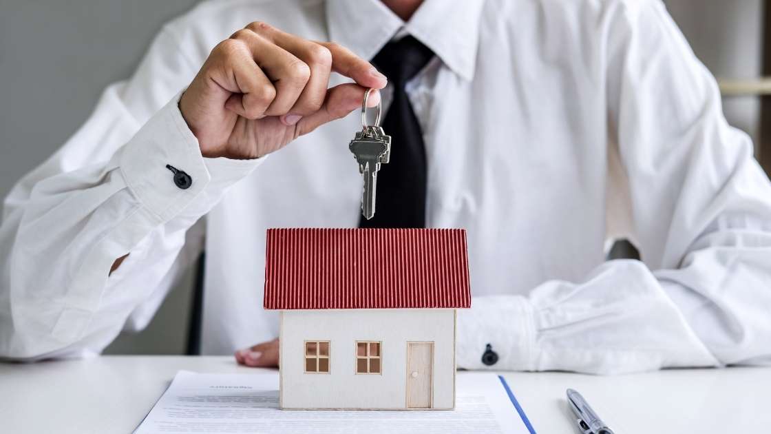 man holding keys above toy home