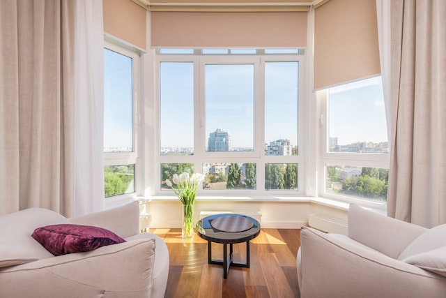 Wide shot of a living room with white furniture and windows looking out onto the city